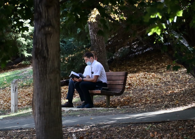 Two LDS Missionaries sitting on a park bench reading the Book of Mormon.