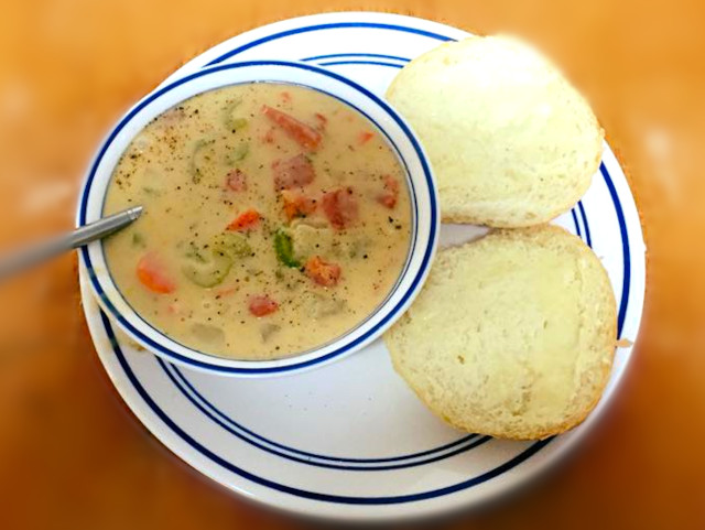 A steaming bowl of potato cheddar chowder and a fresh dinner roll.