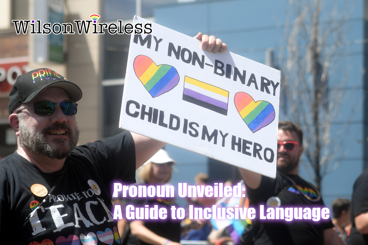 A photo of a parent holding a sign that reads, My non-binary child is my hero, the sign also contains a non-binary flag and two rainbow hearts.